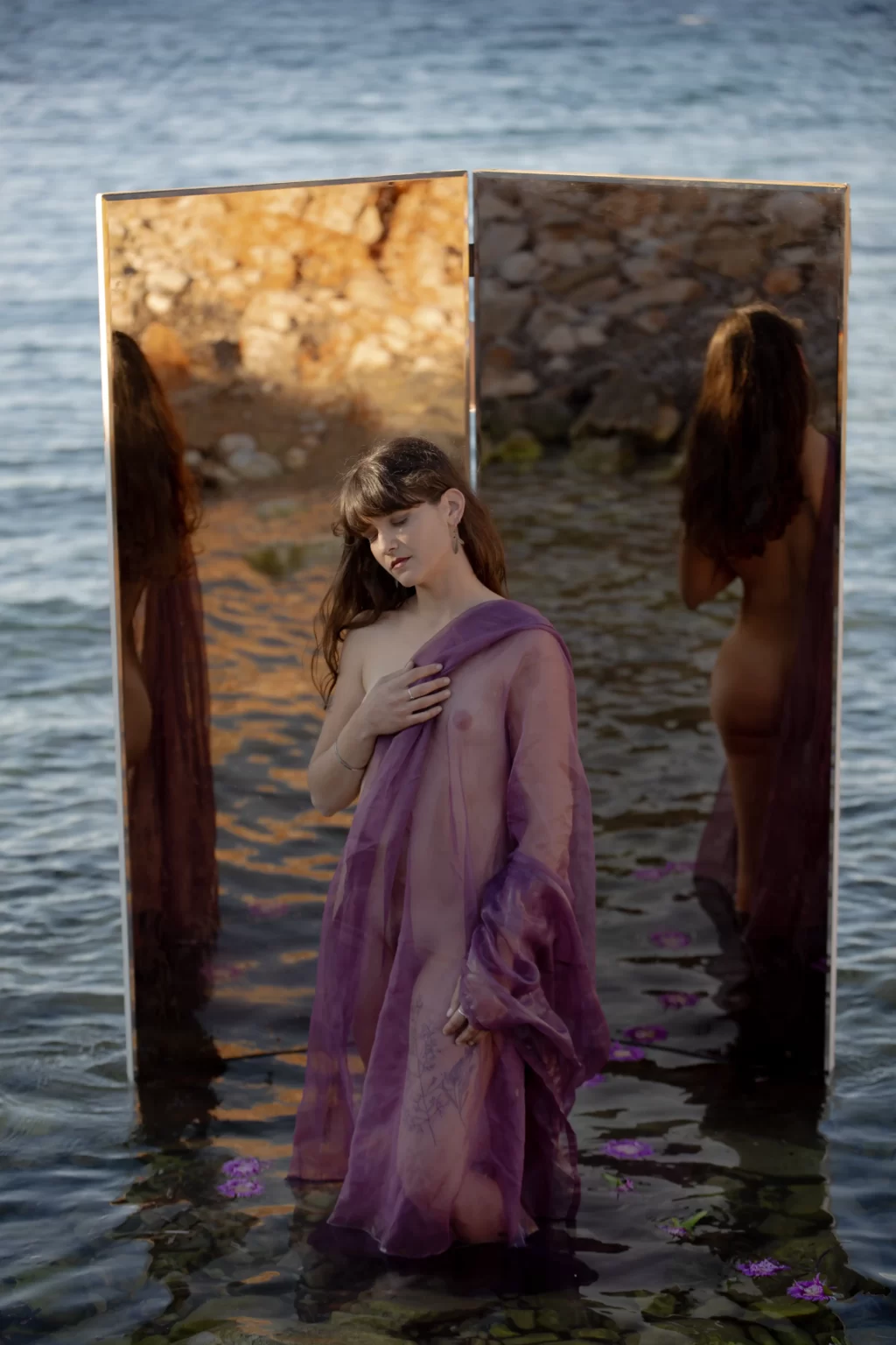 Captivating photograph of Elisavvet resembling Aphrodite, standing by a mirror immersed in the serene waters of a Paros Island beach – a stunning portrayal of Paros' enchanting beauty