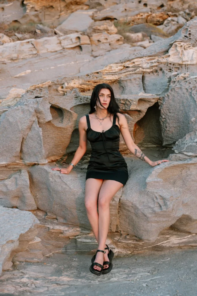 Stunning photoshoot on Paros Island, featuring a woman gracefully posing on the rocky shoreline of a pristine beach. This captivating image is the work of Athens and Paros local photographer, Pranvera Dautllari, showcasing the beauty of Paros through her lens.