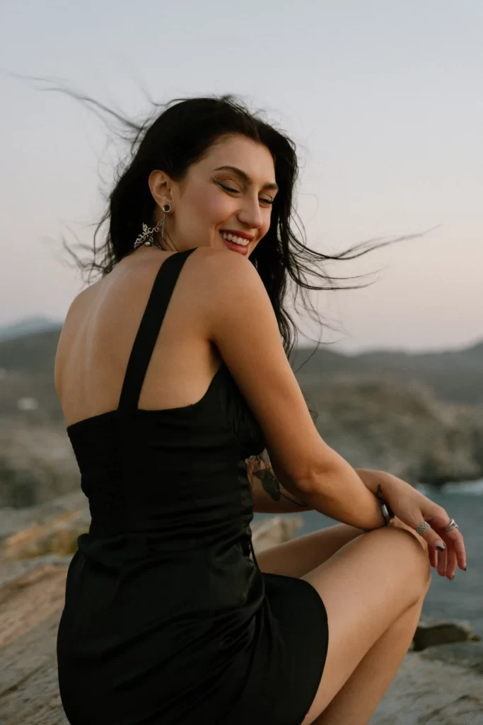 Scenic photoshoot on Paros Island featuring a woman gracefully posing on the beach's rocky shores. Captured by Pranvera Dautllari, a talented local photographer from Athens and Paros
